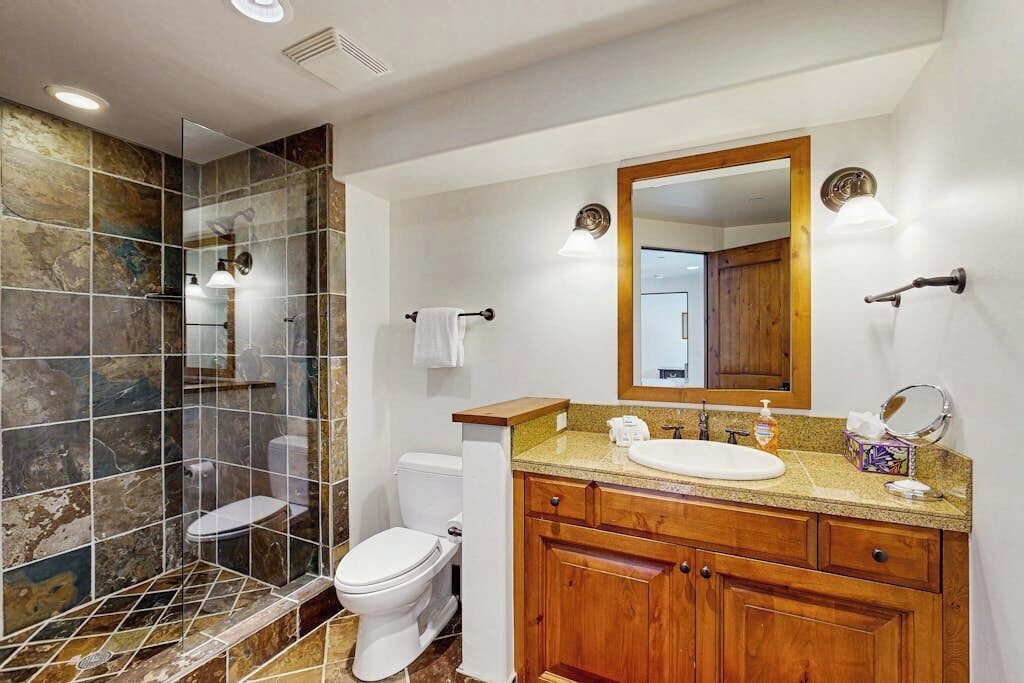 Une salle de bain équipée d’une douche, de toilettes, d’un lavabo et d’un meuble-lavabo en bois.
