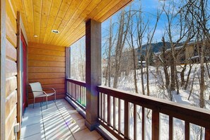 A wooden balcony with a view of snow-covered trees and a distant building. - Spacious mountain getaway near the slopes with riverfront view & garage (Ketchum Idaho)