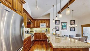 Cocina con armarios de madera, refrigerador de acero inoxidable, encimera de granito e iluminación colgante.