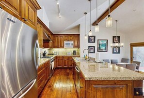 A kitchen with wooden cabinets, a stainless steel refrigerator, a granite countertop, and pendant lighting. - Spacious mountain getaway near the slopes with riverfront view & garage (Ketchum Idaho)
