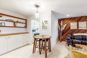 Eine moderne Küche mit weißen Schränken, einer Holzauskleidung und einem Essbereich mit rundem Tisch und Hockern.