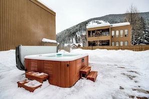 Ein hölzernes Whirlpool in einer verschneiten Außenanlage mit einem Gebäude im Hintergrund.