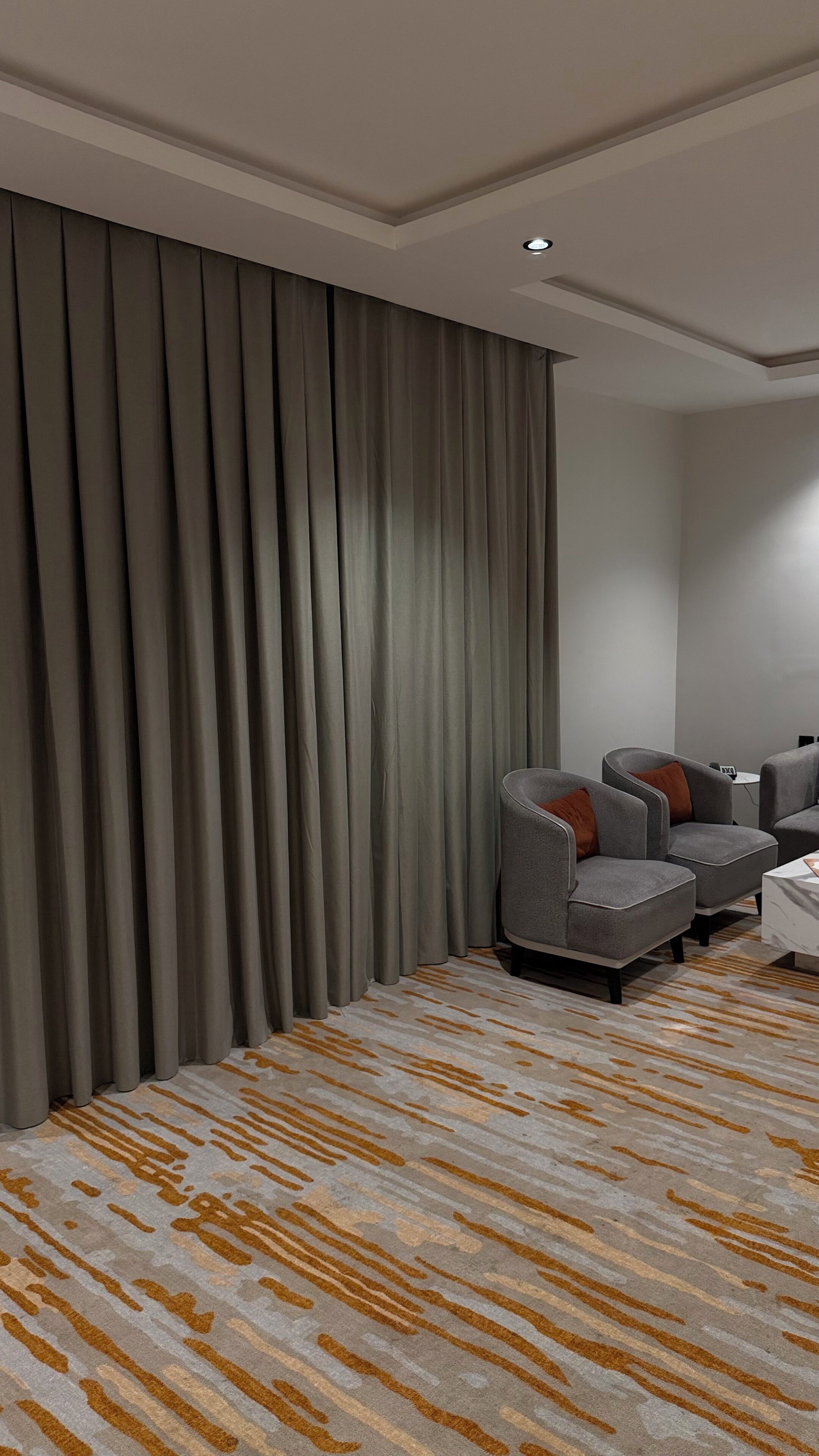 A modern room with grey curtains, a patterned carpet, and two grey armchairs with orange cushions.