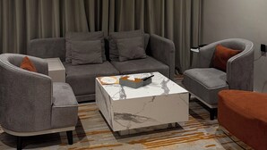 Un salon moderne avec un canapé gris, deux fauteuils, une table basse et un tapis à motifs.