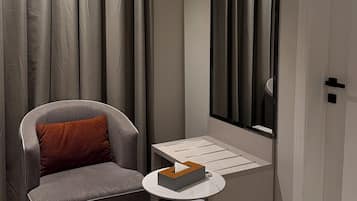 Ein modernes Zimmer mit einem grauen Sessel, einem kleinen runden Tisch mit einer Taschentuchbox, einem großen Spiegel und einer Tür.