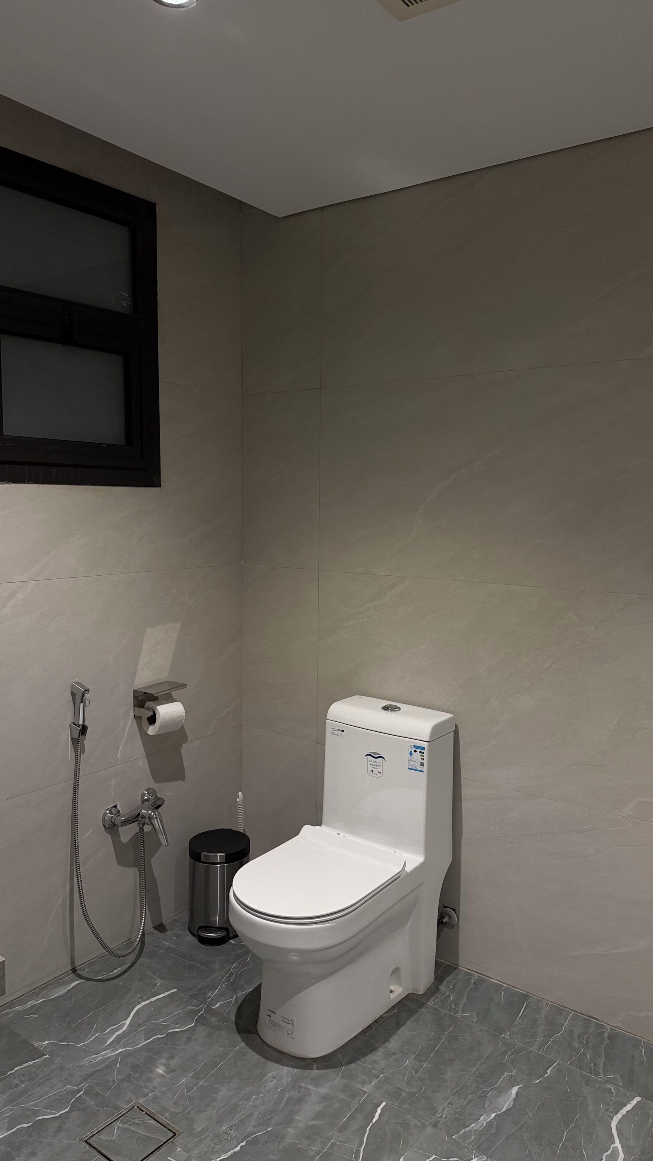 A bathroom with a toilet, a shower, and a trash bin.