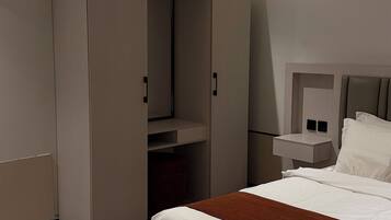 Una habitación de hotel con cama, armario, mesita de noche y estante empotrado.