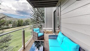 Ein Balkon mit einer Couch, Korbstühlen, einer Glastür und Blick auf eine gebirgige Landschaft.