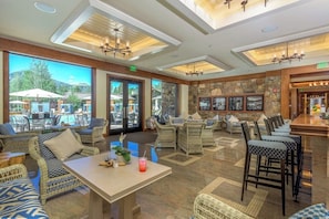 A spacious indoor area with wicker furniture, a bar area, and large windows offering a view of outdoor seating. - Golf course condo with ski shuttle, shared pools, & hot tub (Sun Valley)
