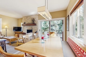 A dining area with a long table, chairs, a television, and a stone fireplace. - Golf course condo with ski shuttle, shared pools, & hot tub (Sun Valley)