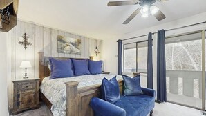 Een slaapkamer met een bed, een blauwe bank, een plafondventilator en een groot raam met gordijnen.