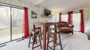 Een woonkamer met een open haard, een tv boven de haard, een eettafel met krukken, en een bank.