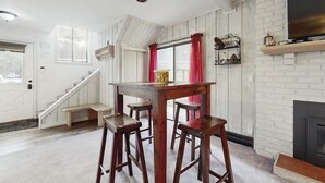 Een kamer met een houten tafel, barstoelen, een open haard, een televisie en een trap.
