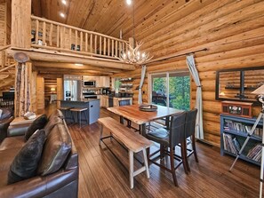 Ein Holzblockhaus-Interieur mit Essbereich, Küche und einem Schlafboden mit Geländer.