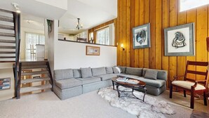 A living room with a grey sectional sofa, a wooden wall, and a staircase. - Wonderful Mountain Getaway W/ Shared Pool, Multiple Balconies, Gas Grill & WiFi (Ketchum)