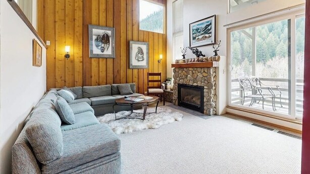 A living room with a stone fireplace, a large window, and a wooden wall. - Wonderful Mountain Getaway W/ Shared Pool, Multiple Balconies, Gas Grill & WiFi (Ketchum)