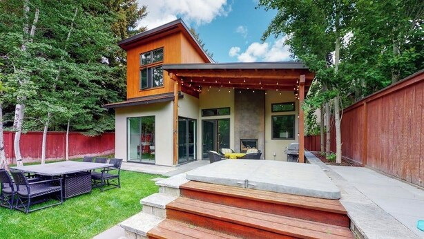 Una casa moderna de dos pisos con un patio, mobiliario exterior y una chimenea de piedra.
