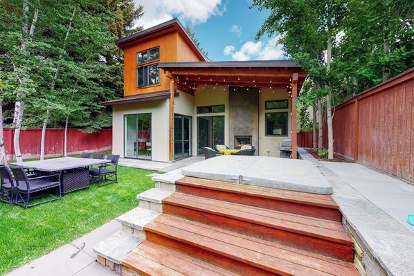 Ein modernes, zweistöckiges Haus mit Terrasse, Außenmöbeln und einem Steinkamin.