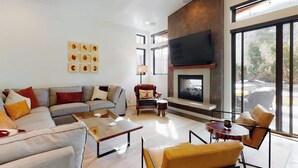Una sala de estar moderna con un sofá modular, una chimenea, un televisor y ventanas amplias.