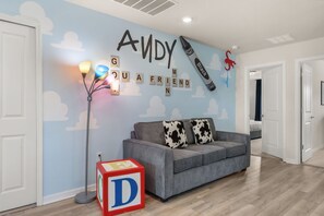A room with a blue wall, a grey sofa, a lamp, and a letter block. - 5 BD/ 4.5 BA Windsor Cay (1276 BP) (Clermont)