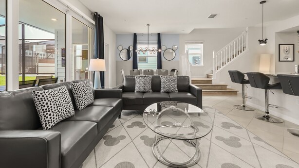 A modern living room with a sectional sofa, a glass coffee table, and a dining area with bar stools. - 5 BD/ 4.5 BA Windsor Cay (1276 BP) (Clermont)