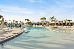 Uma piscina ampla e cristalina, com espreguiçadeiras e palmeiras, emoldurada por um edifício com estilo de resort.