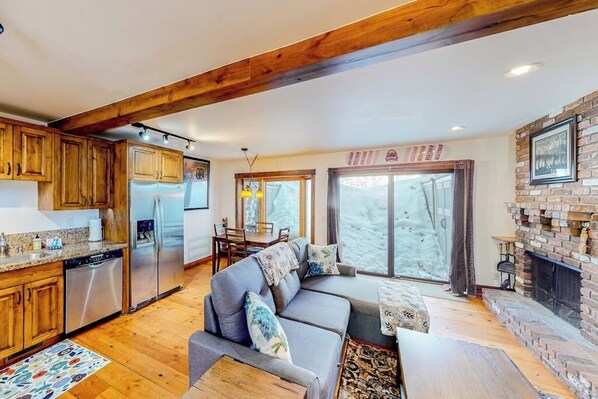 Eine moderne Küche mit Holzausstattung und Edelstahlgeräten, ein gemütlicher Sitzbereich mit einer Couch und Kissen sowie ein Kamin.