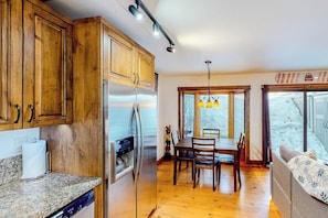 Eine Küche mit Holzausstattung, einem Edelstahlkühlschrank, einem Esstisch mit Stühlen und einem Fenster mit Blick auf eine verschneite Landschaft.