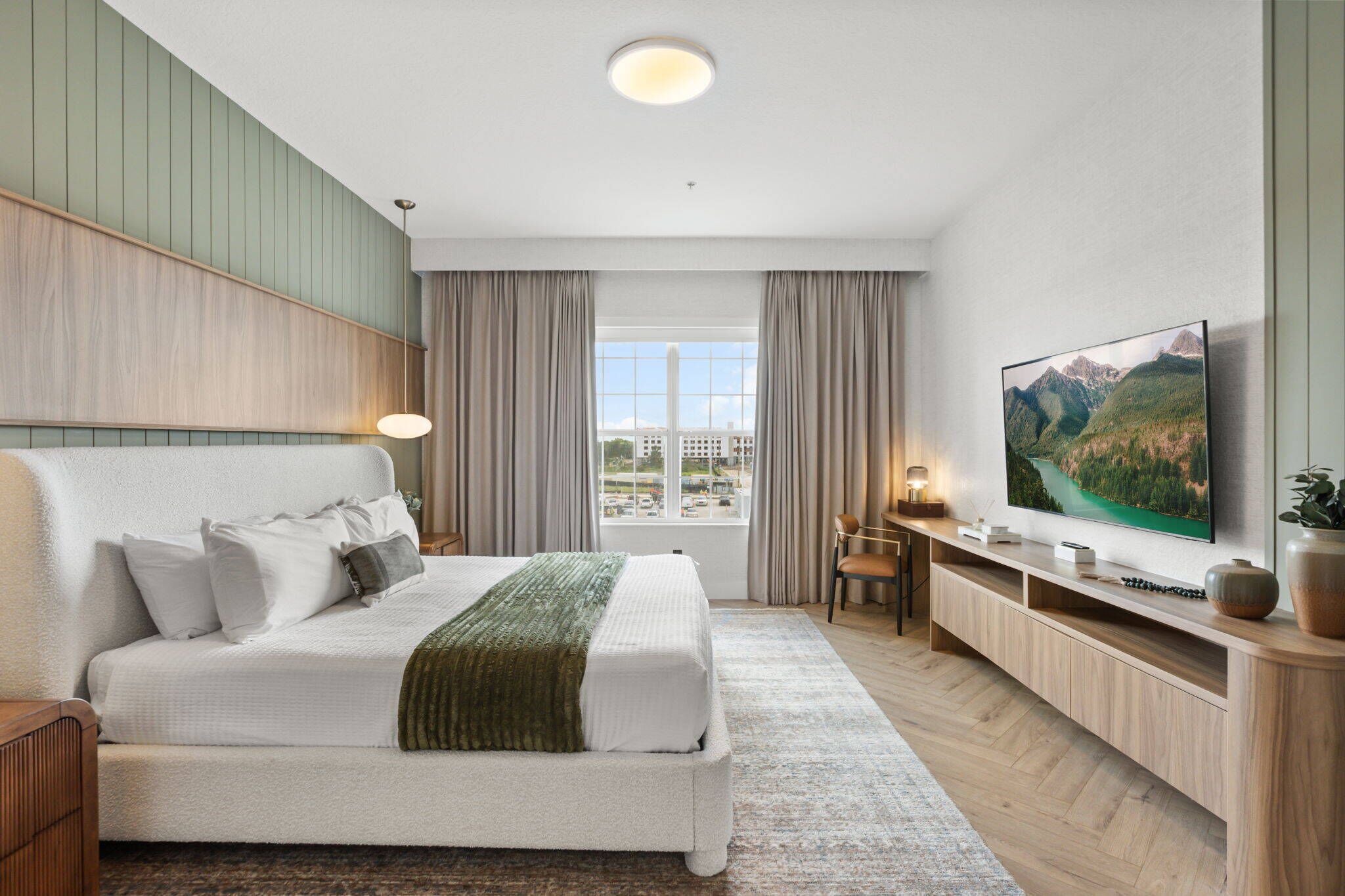 Quarto de hotel moderno com uma cama grande, uma televisão, uma escrivaninha e uma janela com vista para a cidade.