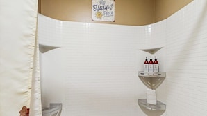 Een badkamer met witte betegelde wanden, een douchegordijn, een handdoekhouder en een plank met toiletartikelen.