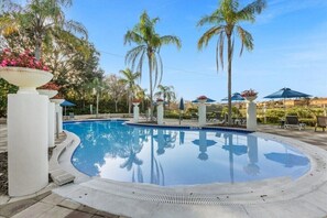 Ein Poolbereich mit Palmen, Liegestühlen und Sonnenschirmen.