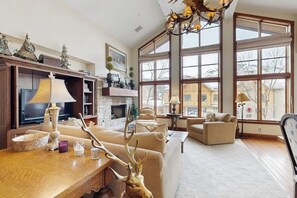 Ein geräumiges Wohnzimmer mit Kamin, großen Fenstern und einer Kristallleuchter.