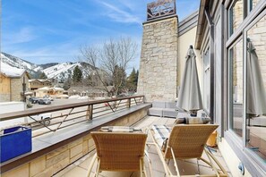Ein Balkon mit Korbstühlen, einer Steinmauer und Blick auf einen verschneiten Berg.