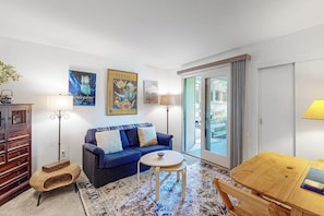 Ein Wohnzimmer mit blauem Sofa, einem kleinen runden Tisch, einem Holzkasten und einem großen Fenster mit Blick.