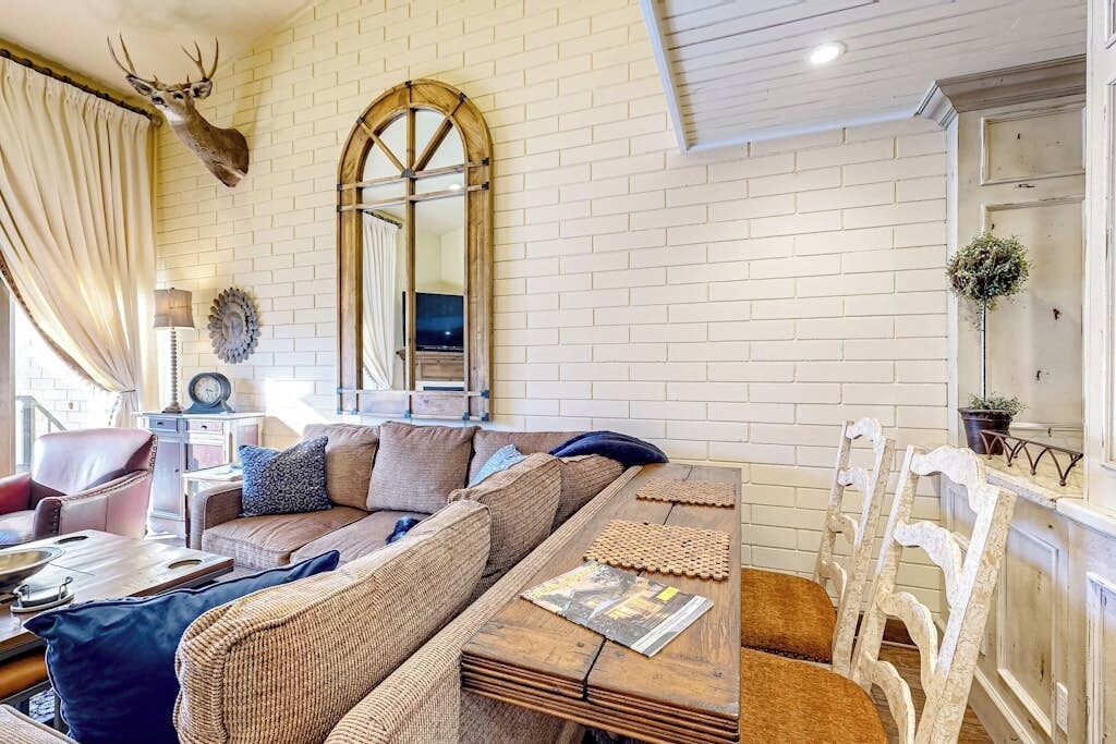 Een woonkamer met een bakstenen muur, een opgehangen hertshoofd, een bank, een salontafel en een spiegel.