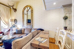 Ein Wohnzimmer mit Backsteinwand, einem aufgehängten Hirschkopf, einem Sofa, einem Couchtisch und einem Spiegel.