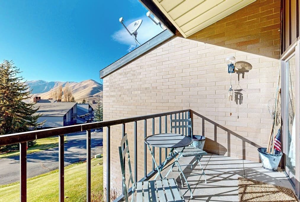 A balcony with a table and chairs, a view of mountains, and a clear sky.