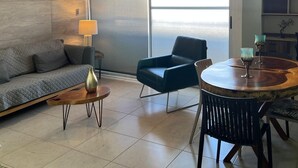 A modern living room with a sofa, a dining table with chairs, a ceiling fan, and a large window with a view. - Modern 2BR 2BA | Workspace Wifi | Pools | 24/7 Sec (Cancún)