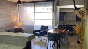 A modern living room with a dining area, a large window, and a ceiling fan. - Modern 2BR 2BA | Workspace Wifi | Pools | 24/7 Sec (Cancún)