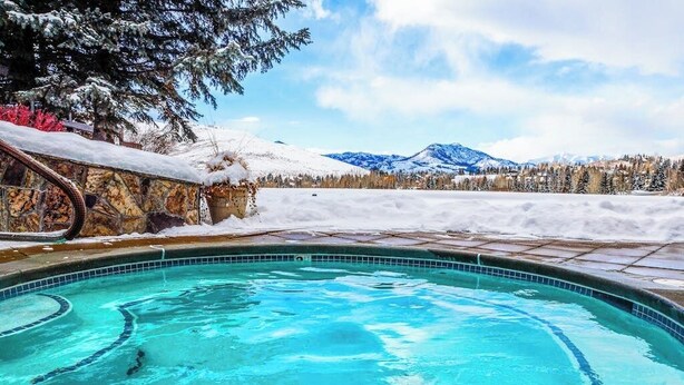 Une piscine bordée d’un mur en pierre, offrant une vue sur des montagnes enneigées.