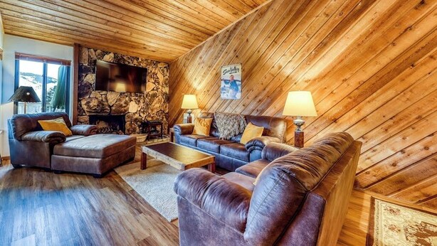 A cozy living room with a stone fireplace, wooden ceiling, and leather sofas. - Mountain retreat with golf on-site (Sun Valley)