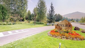 A road sign with 'ATELIER' in the center, surrounded by a flower bed and trees.