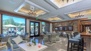 A spacious indoor area with wicker furniture, a bar, and large windows overlooking an outdoor pool area.