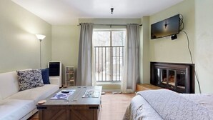 Una habitación con sofá, una mesa de centro, televisor montado en la pared, chimenea y ventana con cortinas.