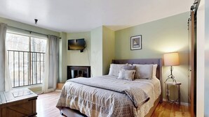 Un dormitorio con cama, mesita de noche, lámpara, televisor y ventana con cortinas.