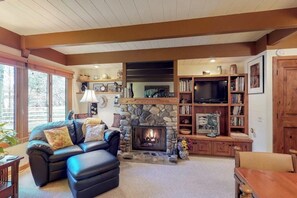 A cozy living room with a stone fireplace, leather sofa, and wooden bookshelves. - Charming condo w/ full kitchen, washer/dryer - close to ski slopes (Sun Valley)