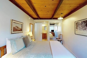 A bedroom with a wooden ceiling, a bed with a white and blue bedspread, a chair, and a framed picture on the wall. - Bright Condo Less than a Mile to Ski Lifts, Pool, Tennis (Sun Valley)