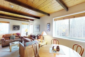 A cozy living room with a wooden ceiling, leather sofas, a round dining table, and large windows with a view of trees. - Bright Condo Less than a Mile to Ski Lifts, Pool, Tennis (Sun Valley)