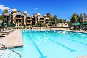 A swimming pool with lounge chairs and umbrellas, surrounded by multi-story buildings with balconies. - Bright Condo Less than a Mile to Ski Lifts, Pool, Tennis (Sun Valley)
