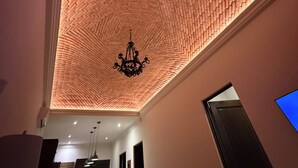 Une pièce avec un plafond orné d’un motif en briques, un lustre et un coin repas comprenant une table et des chaises.